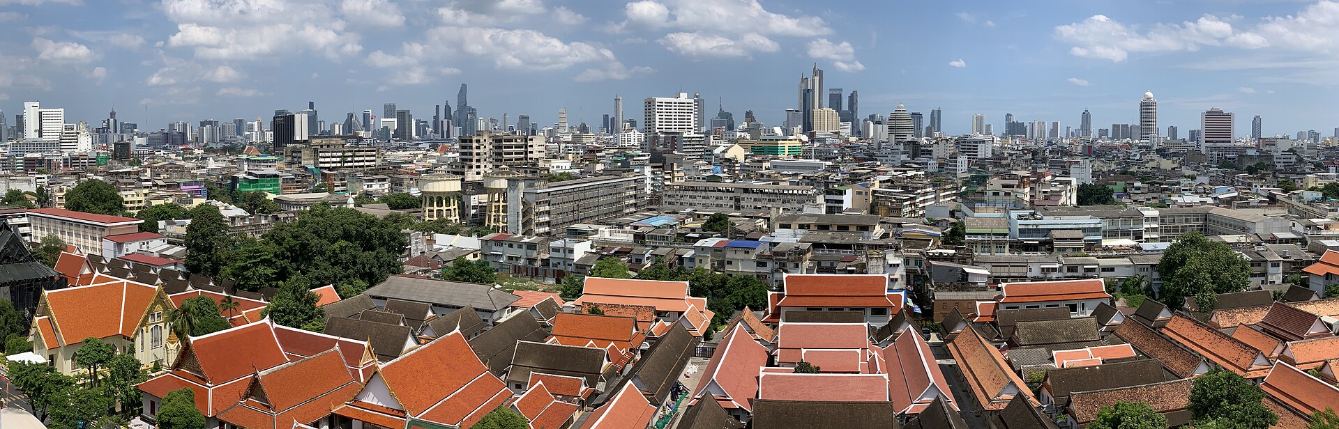 Bangkok, les toits rouges d'un temple au premier plan et les tours du centre derrière